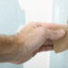 Man's hand sanding plaster on a new new drywall installation.  Hands are dirty and worn from work.