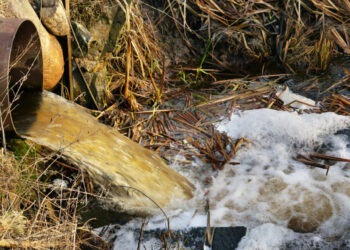 Dirty waste water merges into a clean forest stream. Landscape concept - pollution of the environment. Winter european landscape